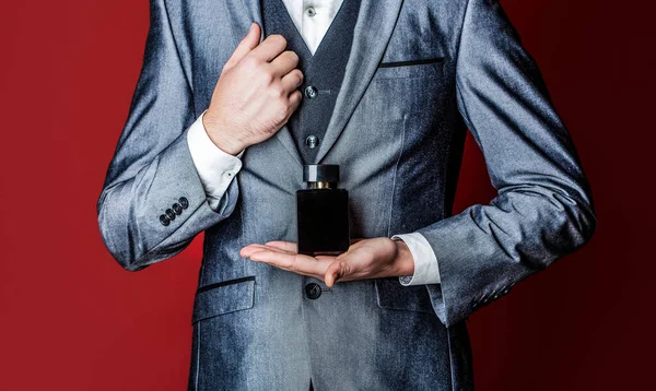Man in formal suit, bottle of perfume, closeup. Man holding up bottle of perfume. Men perfume in the hand on suit background. Fragrance smell — Stock Photo, Image