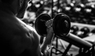 Vücut geliştirici, dambıllarla egzersiz yapıyor. Vücut geliştirici spor salonunda halterlerle çalışıyor.