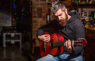 Canlı müzik. Gitarlar ve teller. Gitar çalan sakallı bir adam, elinde akustik bir gitar tutuyor. Müzik konsepti. Sakallı gitarist. Gitar çal. Sakallı hippi barda oturuyor.