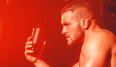 Genç adam spor salonunda su içer. Spor salonunda elinde su şişesi olan bir adam. Spor salonunda su içen yakışıklı kaslı adamın yaşam tarzı portresi. Kaslı adam su içiyor. Şişede su var.