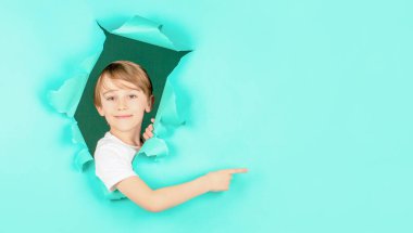 Çocuk delikten bakıyor. Sarışın çocuk yırtık kağıda bakıyor. Kırmızı kağıt delikteki çocuk parmağıyla işaret ediyor. Kağıt duvardaki delikten bakan gülümseyen çocuk. Şaşırmış çocuk kağıtta delik açıyor.
