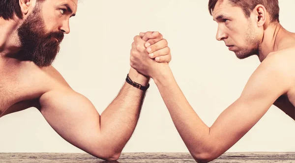 Two mans hands clasped arm wrestling, strong and weak, unequal match. Heavily muscled bearded man arm wrestling a puny weak man. Arms wrestling thin hand, big strong arm in studio — Stock Photo, Image