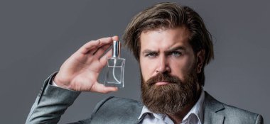 Parfüm, parfüm şişesi, parfüm, kozmetik, parfüm şişesi, erkek parfümü. Erkek parfümü, takım elbiseli sakallı bir adam. Elinde parfüm şişesi tutan bir erkek.