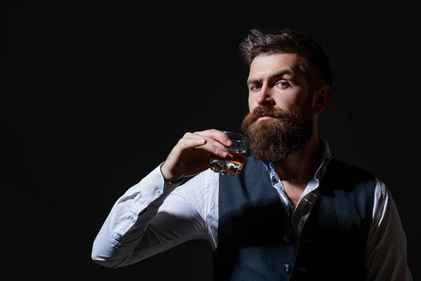 Omul de afaceri cu barbă în costum elegant, cu pahar de whisky. Degustare, degustare. Omul cu barbă ţine pahar de coniac. Conceptul de degustare și degustare — Fotografie, imagine de stoc