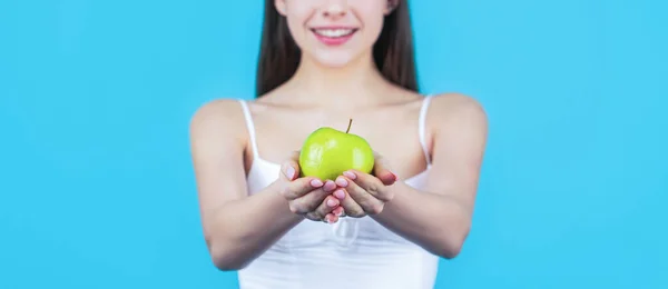 Здоровое питание. Женщина с идеальной улыбкой держит яблоко, синий фон. Женщина ест зеленое яблоко. Портрет молодой красивой счастливой улыбающейся женщины с зелеными яблоками — стоковое фото