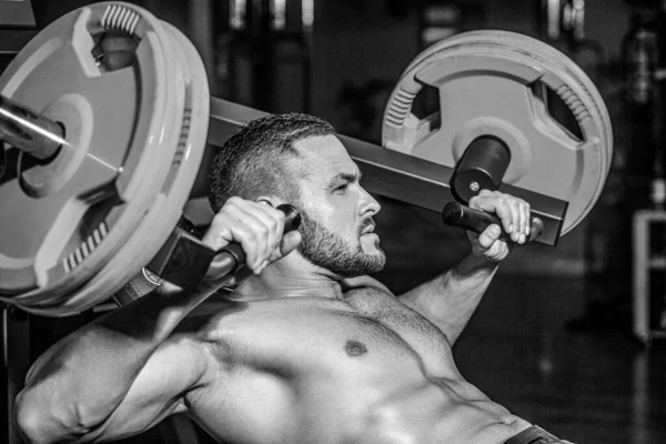 Spor salonunda halterle çalışan kaslı bir adam. Vücut geliştirici atletik adam, karın kasları, omuzları, pazıları, kol ve göğsü mükemmel. Koltuk değneği egzersizi. Atletik adam halterli, spor salonunda çalışıyor.