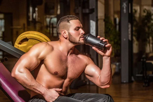 Muscular man drinking water. Holding bottle waters. Young man drinks water in the gym. Man at gym and holding bottle of water. Lifestyle portrait of handsome muscular man drinking water in the gym.