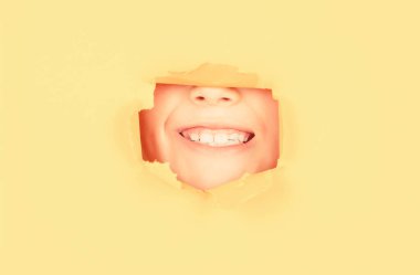 Kırıcı kağıt arkaplan. Duygular konsepti. Yüzü kağıt delikte görünen dişlek gülümsemeli çocuk..