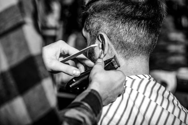 Hands of barber with hair clipper, close up. Haircut concept. Hipster client getting haircut. Black and white.