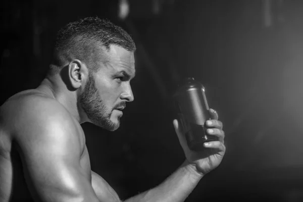 Spor salonunda su içen yakışıklı kaslı adamın yaşam tarzı portresi. Kaslı adam su içiyor. Şişe suyu tutuyorum. Siyah ve beyaz.