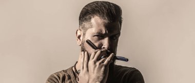 Klasik düz tıraş bıçağı. Erkek tıraşı. Berber dükkanındaki adam. Yakışıklı sakallı kuaför berber dükkanı işletirken elinde jilet tutuyor..