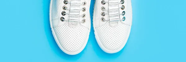 White shoes. Pair of white shoes on blue background. Overhead shot of running shoes. Close up, modern fashion shoes made of laces.