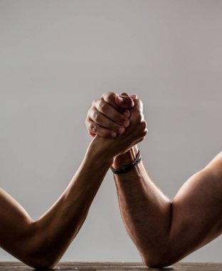 Two mans hands clasped arm wrestling, strong and weak, unequal match. Heavily muscled man arm wrestling a puny weak man.