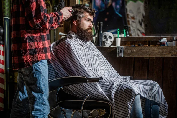 Hands of barber with hair clipper. Bearded man in barbershop. Haircut concept. Man visiting hairstylist in barbershop. Barber works with hair clipper. Hipster client getting haircut.