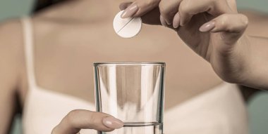 Birkaç hap al, bir bardak su tut. Baş ağrısına karşı ilaç alan genç bir kadın..