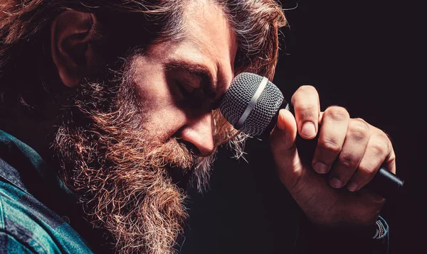 Man with a beard holding a microphone and singing. Bearded man in karaoke sings a song into a microphone. Male singing with a microphones. Male attends karaoke. Bearded man singing with microphone.