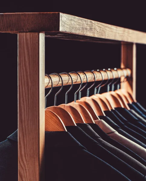 Mens suits in different colors hanging on hanger in a retail clothes store, close-up. Mens shirts, suit hanging on rack. Hangers with jackets on them in boutique. Suits for men hanging on the rack.