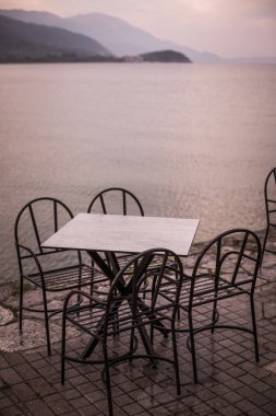 Açık bir terasta, göl kenarında boş sandalye ve masaların renkli görüntüsü.