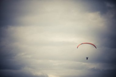 Gri bulutlu gökyüzüne karşı tek başına uçan bir paraglider görüntüsü.