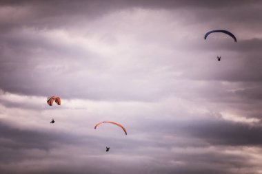 Gri bulutlu gökyüzüne karşı uçan bazı paraşütçülerin görüntüsü.