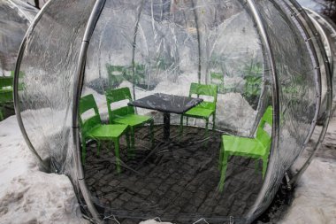 Dışarıdaki bir restoranda dışarıda yemek yemek için kurulmuş bir masanın üzerinde berrak bir plastik kabarcık çadırı görmek..