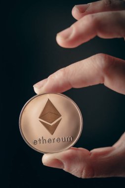 Gümüş bir Ethereum dijital kripto para birimini tutan insan parmaklarını yakından çek.