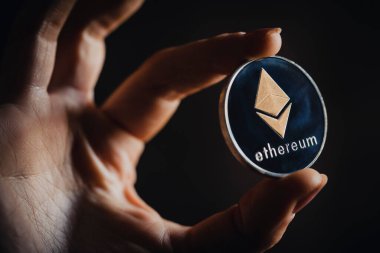 Gümüş bir Ethereum dijital kripto para birimini tutan insan parmaklarını yakından çek.