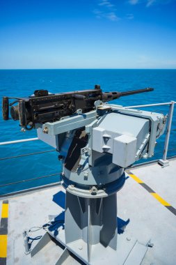 Color image of an automated machine gun on the deck of a military ship, at sea.
