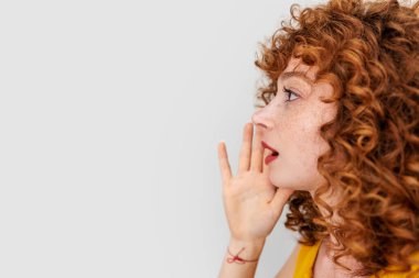 Genç kızıl saçlı kadın elini yüzüne koydu ve beyaz arka planda izole edilmiş birine bağırdı.. 