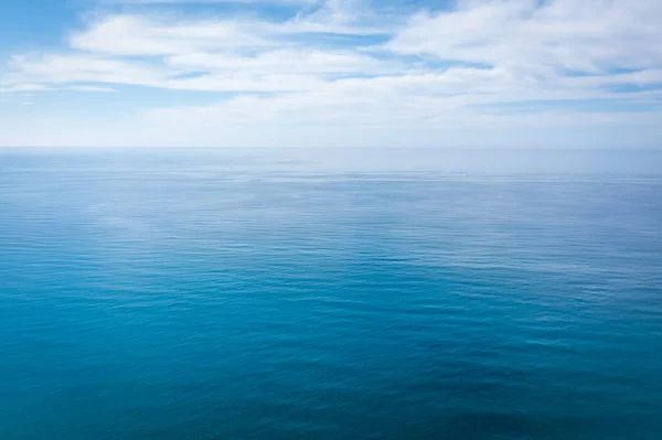 Superfície próxima da calma água do mar azul oceano com luz do dia e nuvens. Textura de fundo abstrata. — Fotografia de Stock