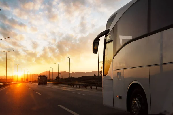Автобус едет по асфальтовому шоссе по сельской местности против заката. Концепция путешествий и транспорта. — стоковое фото