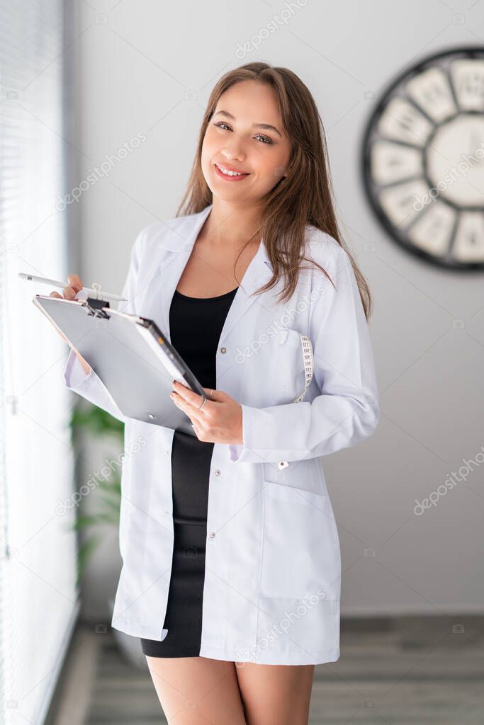 A attractive female dietician doctor is holding a notebook and looking with, confidence and pretty smile.