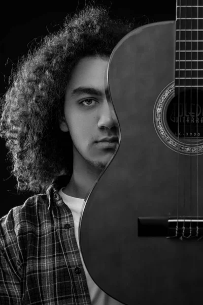 Young man with curly hair is posing with a acoustic guitar in front of his face. Black and white photo. — 스톡 사진