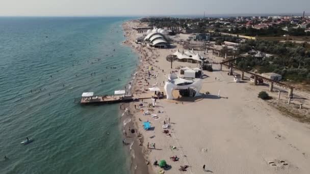 Imágenes de 4k de una playa de arena en la orilla del mar llena de gente. disparos aéreos. — Vídeos de Stock