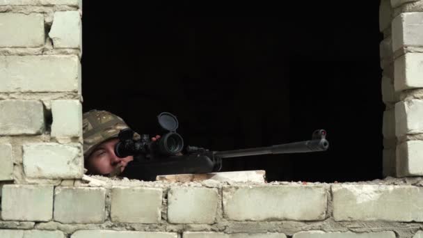 Żołnierz w kamuflażu celuje z okna opuszczonego budynku z karabinem snajperskim — Wideo stockowe