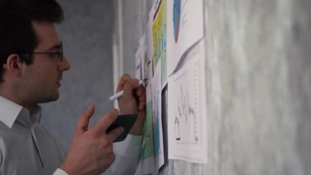 A férfi jegyzetel a falon lévő ábrákon. — Stock videók