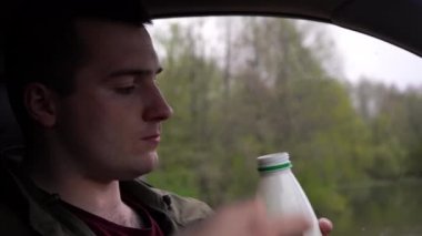 Adam arabada otururken süt içiyor.