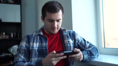 Pencere kenarındaki bir odada konsolu oynayan bir adam.