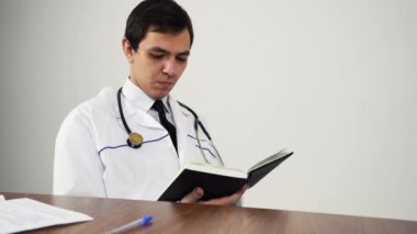 Doktor ofisinde otururken bir kitap okuyor.