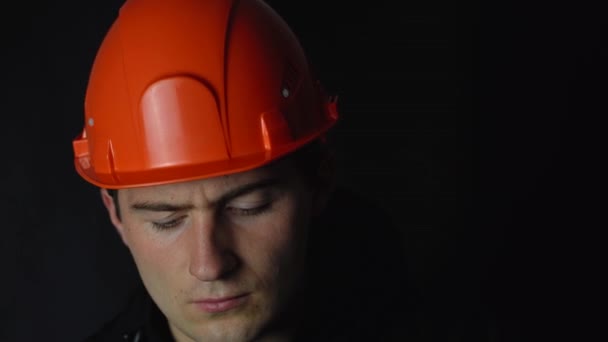 Hombre en casco de construcción naranja sobre fondo negro — Vídeos de Stock