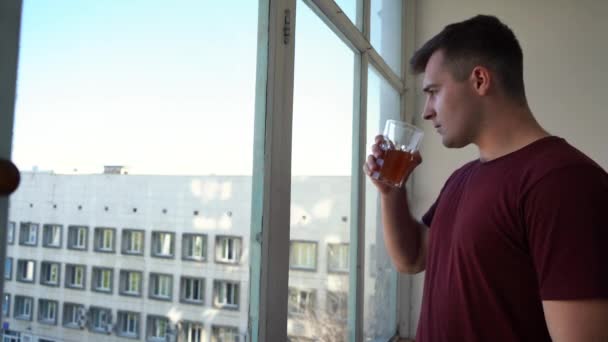 Человек пьет сок из стакана, стоящего на балконе — стоковое видео