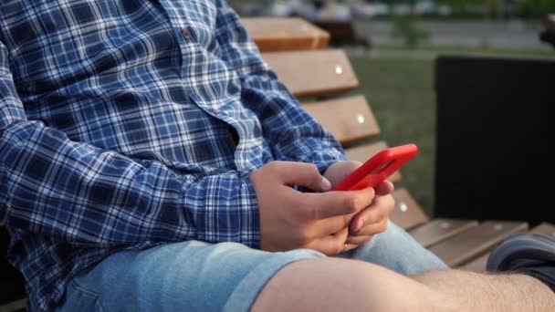 Mann benutzt rotes Telefon, während er auf einer Bank im Park sitzt — Stockvideo