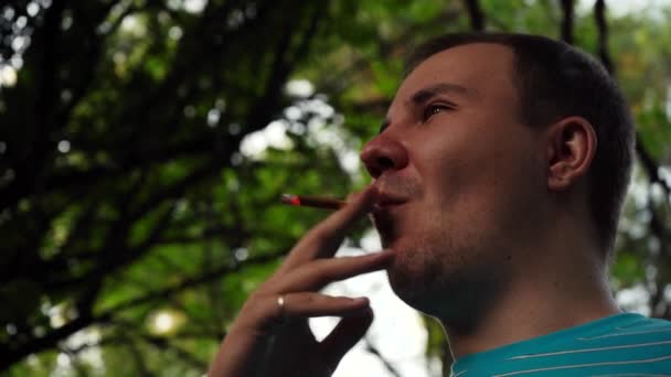 Muž kouří cigaretu na ulici v parku. Záběry 4k zdola — Stock video