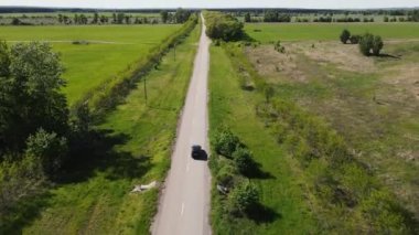 Araba yeşil tarlalar arasında yol boyunca ilerliyor.