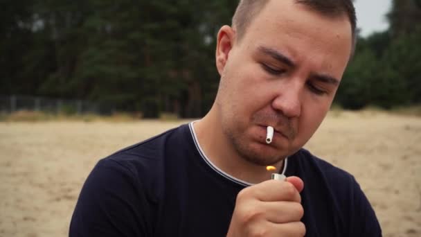 Muž si zapálí cigaretu na pláži. Záběry 4k — Stock video
