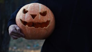 Bir adam ormanda dururken elinde bir balkabağı tutuyor.