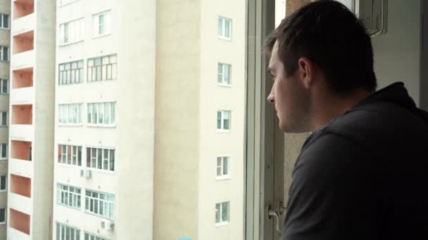 4k Filmmaterial eines Mannes, der aus seinem Wohnungsfenster schaut — Stockvideo