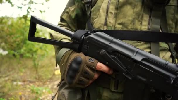 Un soldado bien equipado camina con un arma en sus manos en una zona forestal — Vídeos de Stock