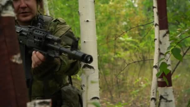Солдат с пулемётом, выглядывающий из-за дерева в лесу — стоковое видео