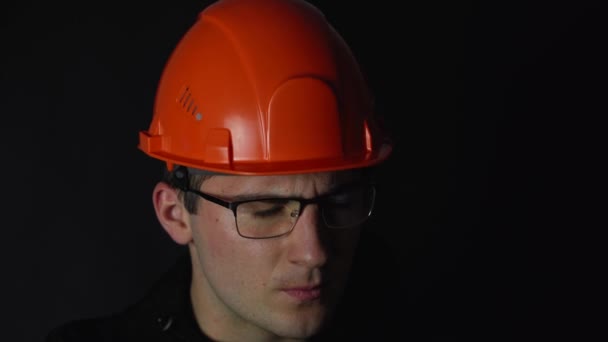 Un hombre con gafas y un casco examina documentos sobre un fondo oscuro — Vídeo de stock